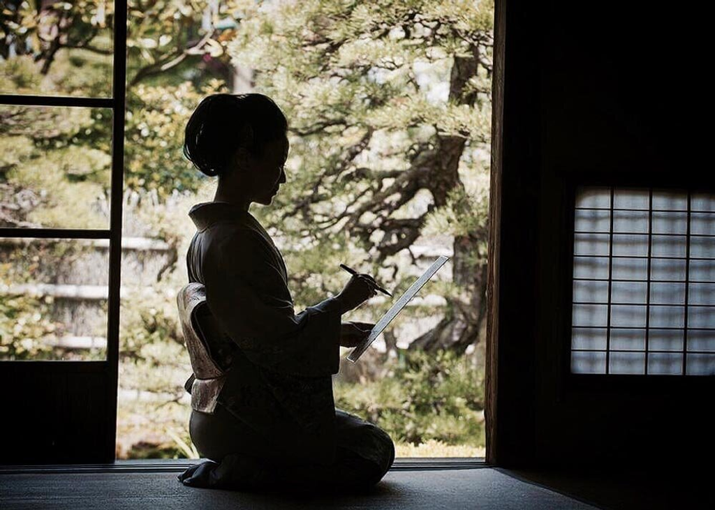 Silhouette of person writing at traditional Japanese doorway overlooking garden.