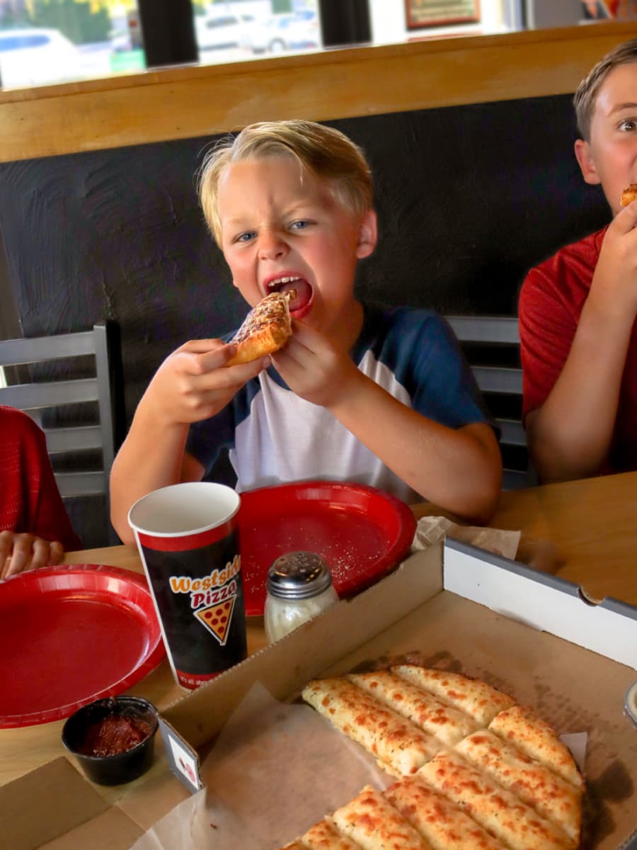 Kid taking a bite out of a slice of pizza from Westside Pizza