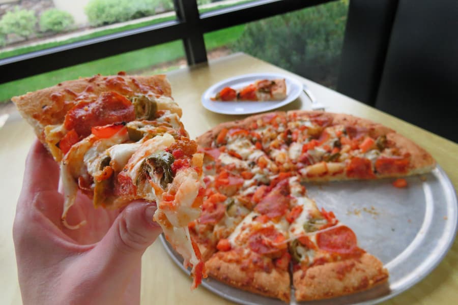 A first person POV holding a slice of pizza at a pizza booth.