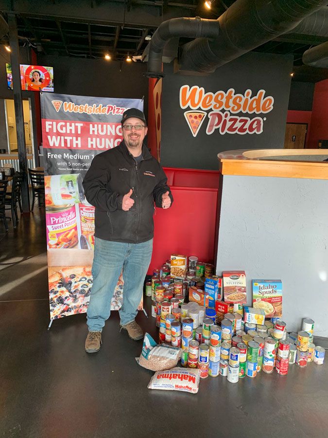 Man Standing in Front of Donated Food | Westside Pizza