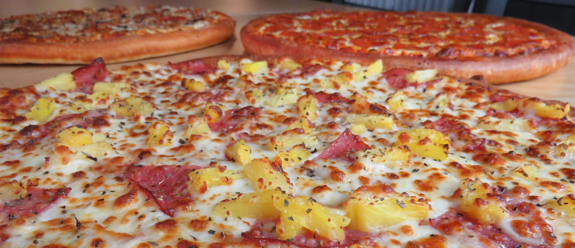 Hawaiian pizza in front of two other pizzas