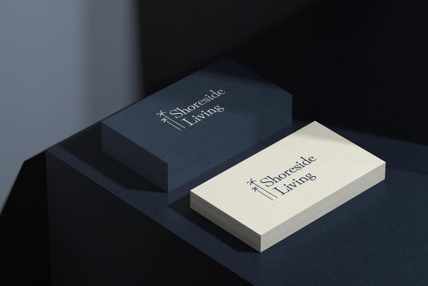 Stacked business cards for Shoreside Living featuring a minimalist navy and cream design with a palm tree logo and elegant serif typography, showcasing custom branding and print design