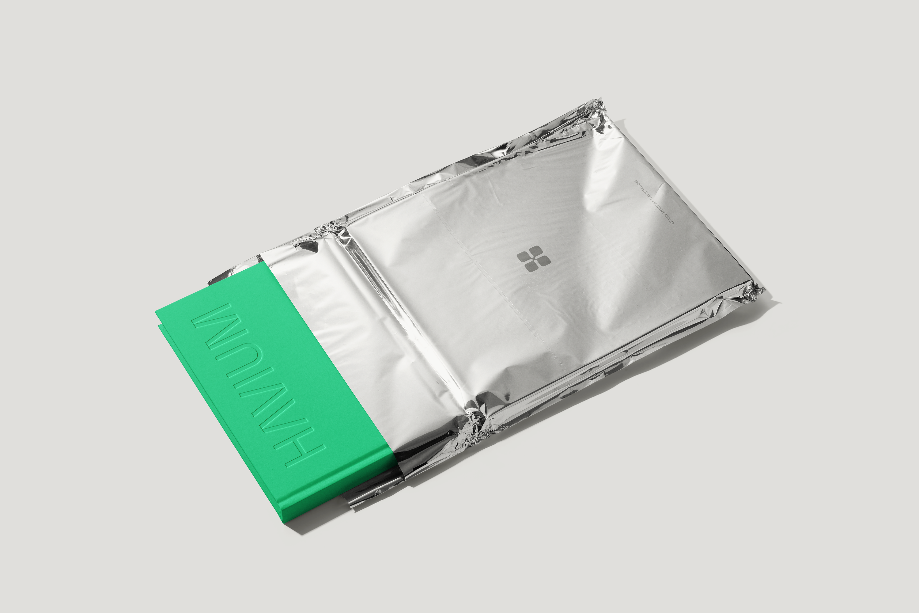Green book with an embossed Havium wordmark, partially enclosed in silver foil packaging bearing the Havium logo.