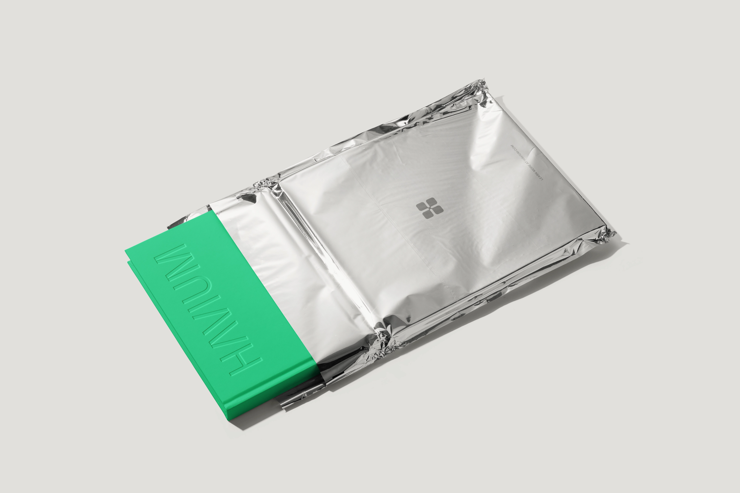 Green book with an embossed Havium wordmark, partially enclosed in silver foil packaging bearing the Havium logo.