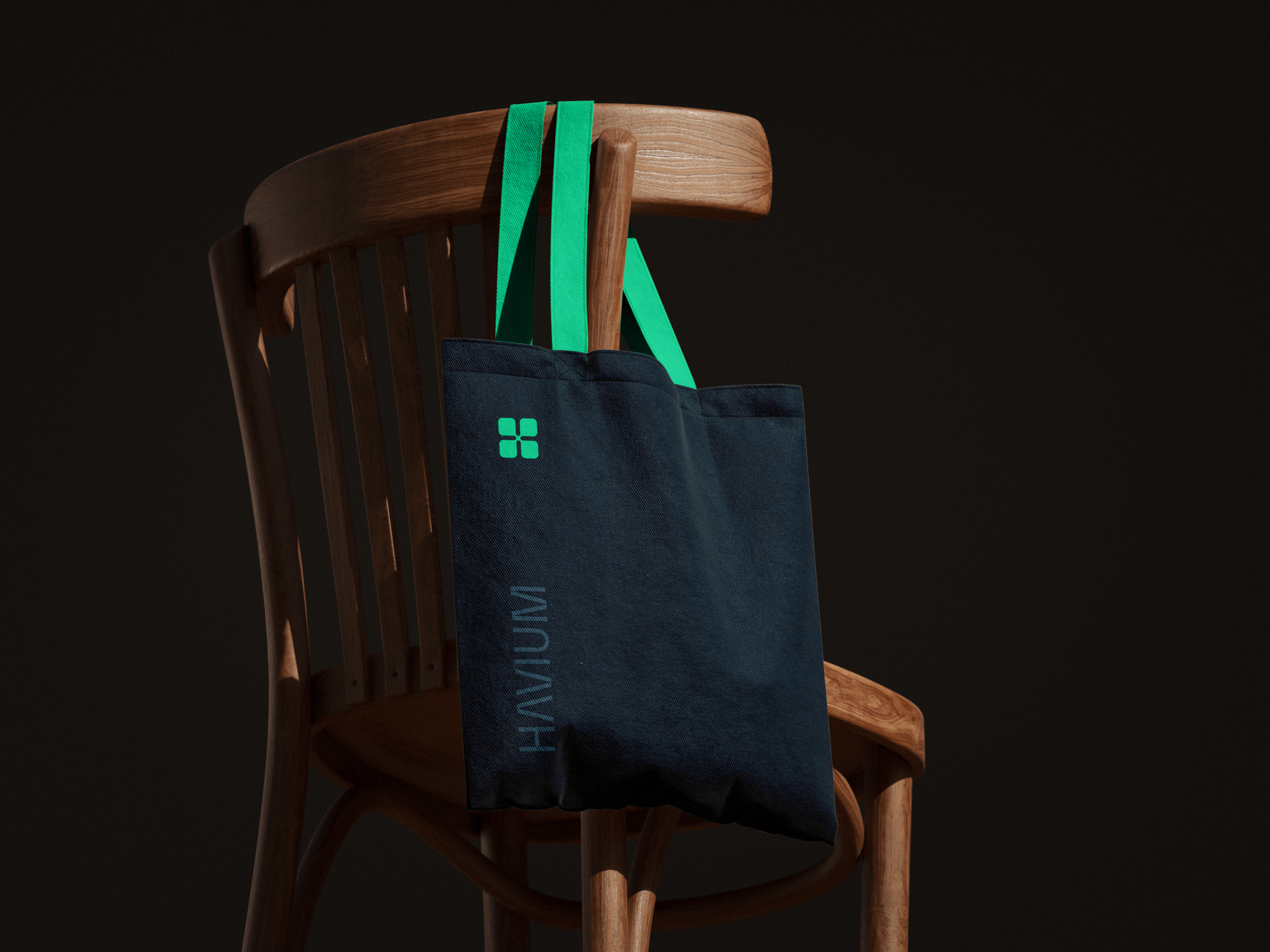 Navy Havium tote bag with green handles and logo, hanging from a wooden chair against a dark background.