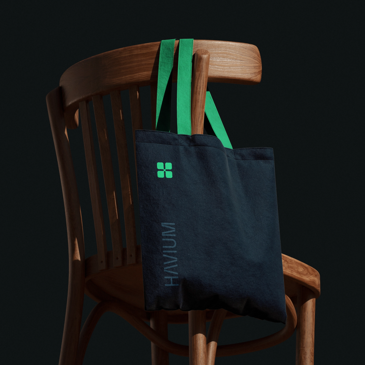 Navy Havium tote bag with green handles and logo, hanging from a wooden chair against a dark background.