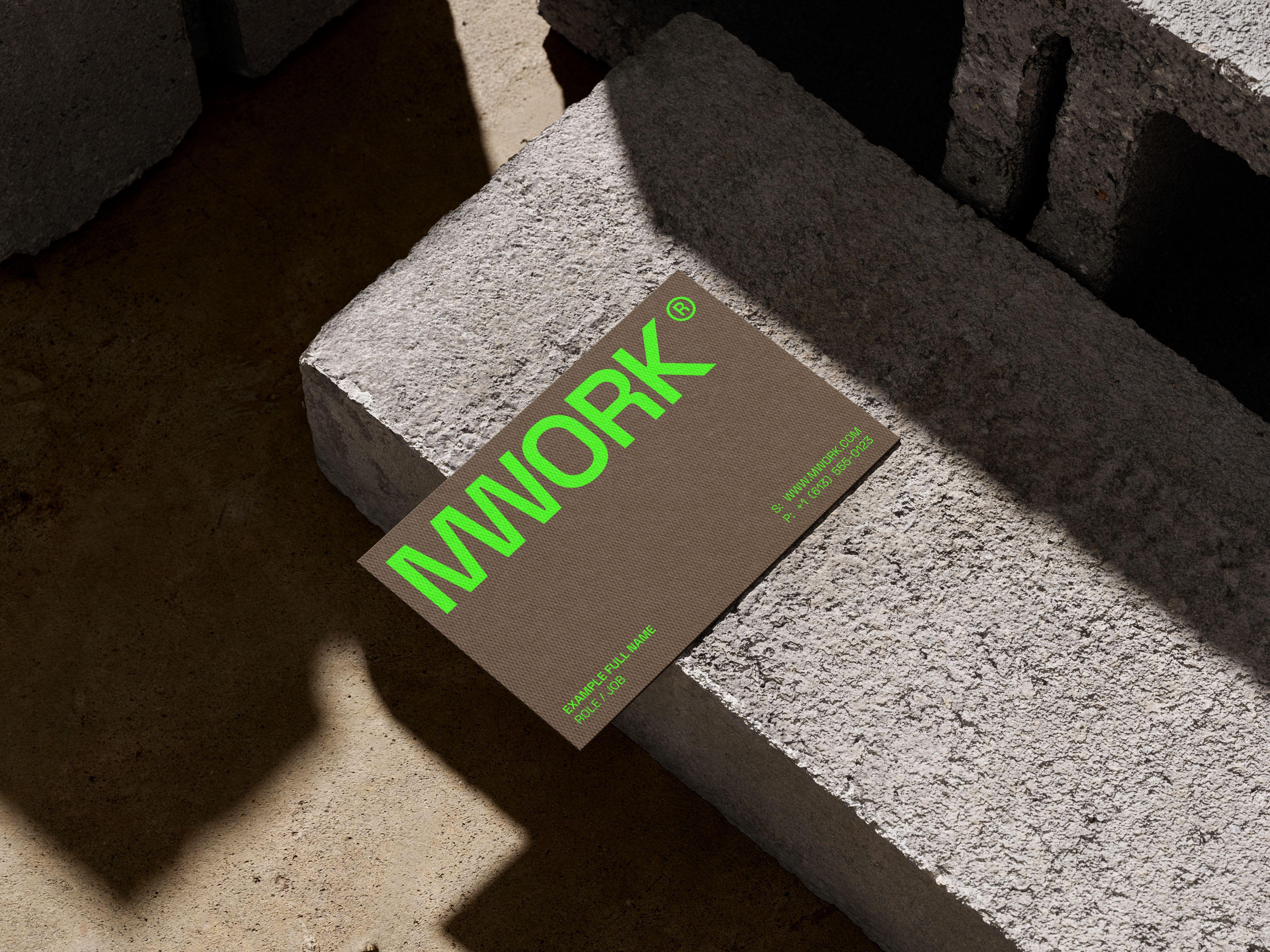 MWORK business card with a large neon green logo panel on a warm brown card, photographed on a concrete surface.