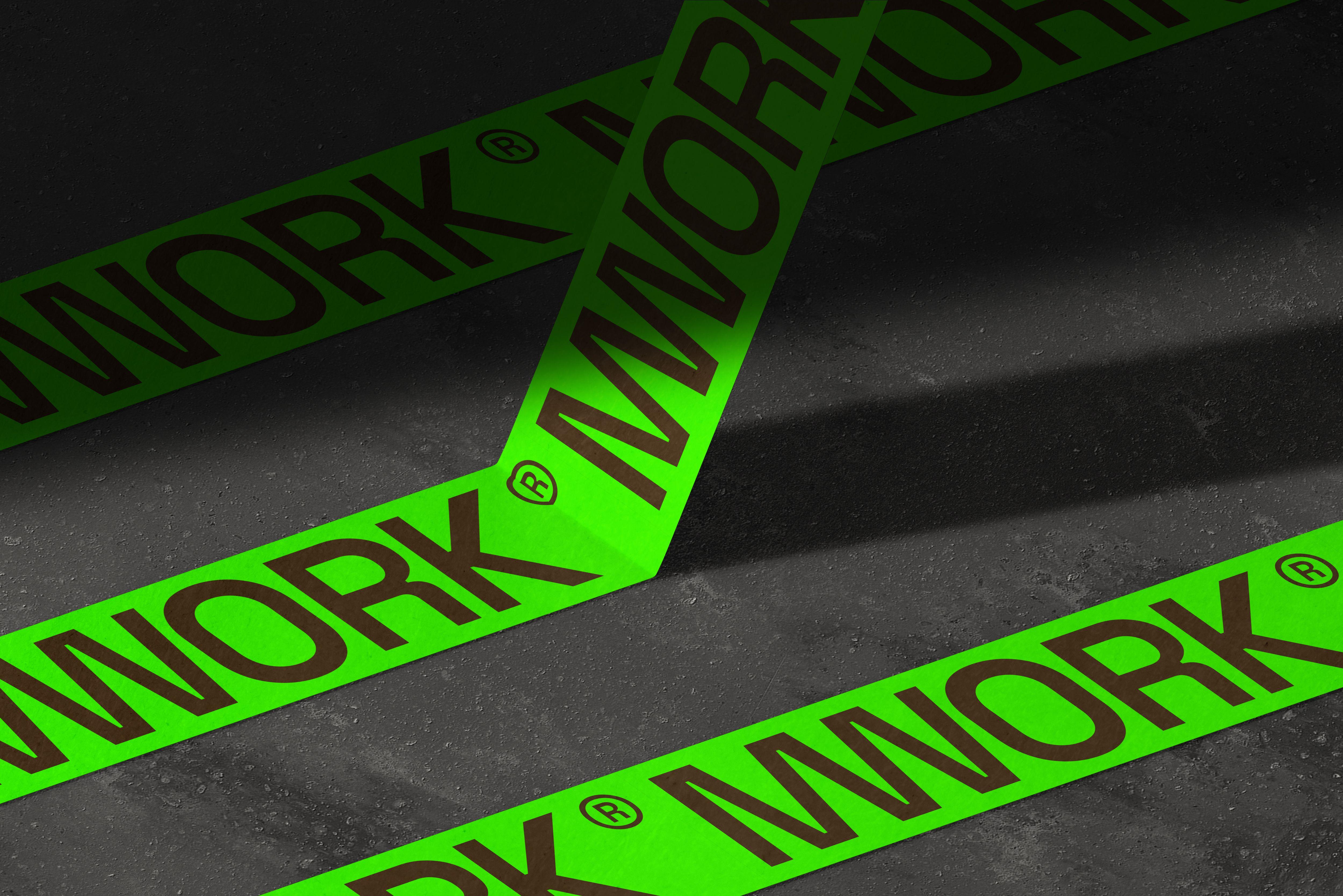 Neon green MWORK branded tape applied directly onto dark pavement at a job site.