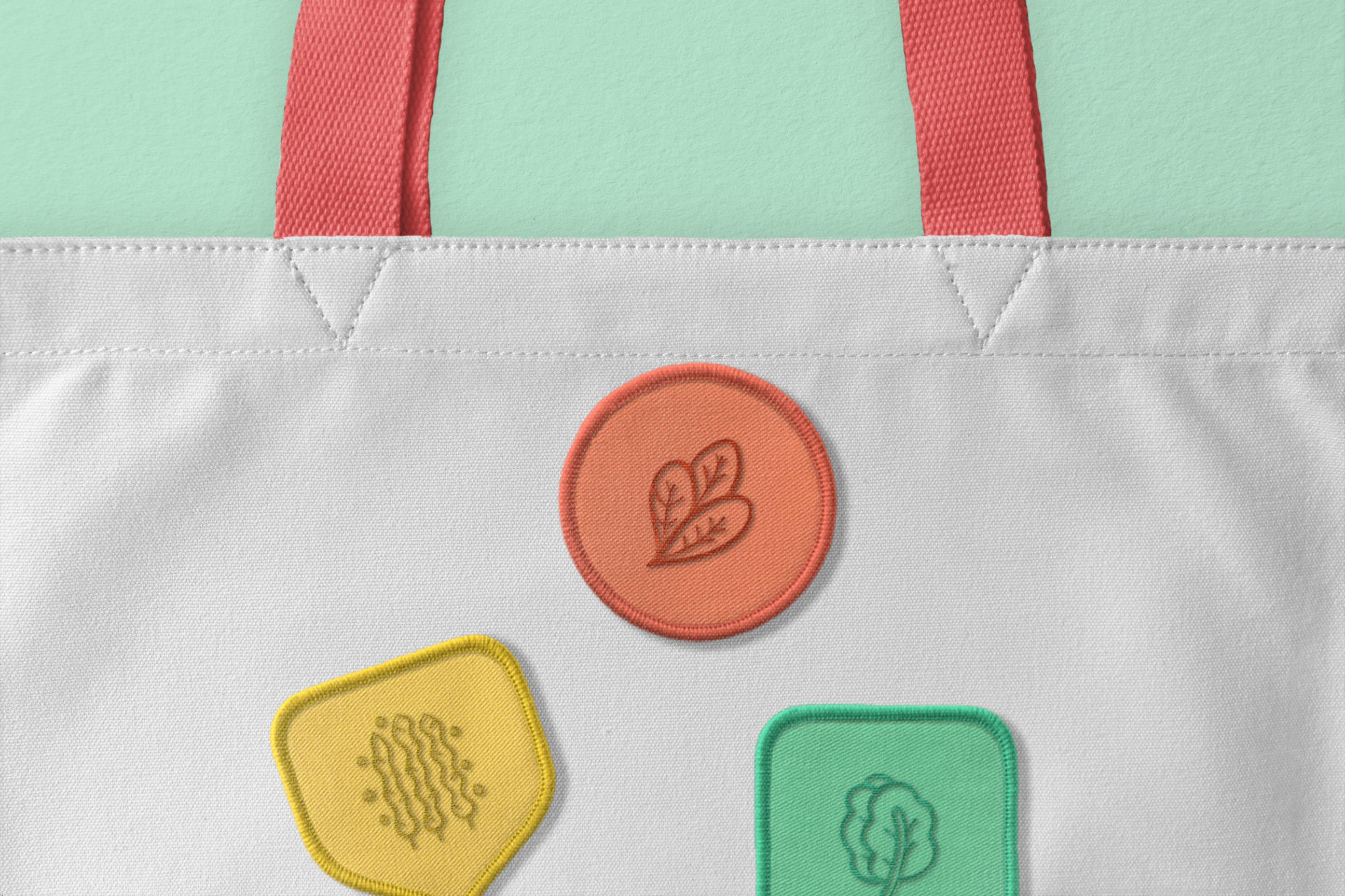 Close-up of a tote bag with colorful embroidered patches representing eco-friendly elements like leaves and vegetables, emphasizing sustainability.