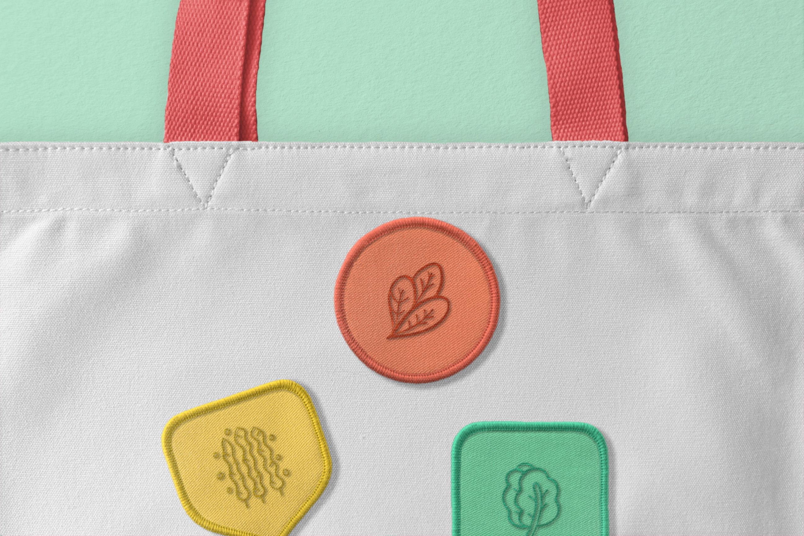 Close-up of a tote bag with colorful embroidered patches representing eco-friendly elements like leaves and vegetables, emphasizing sustainability.