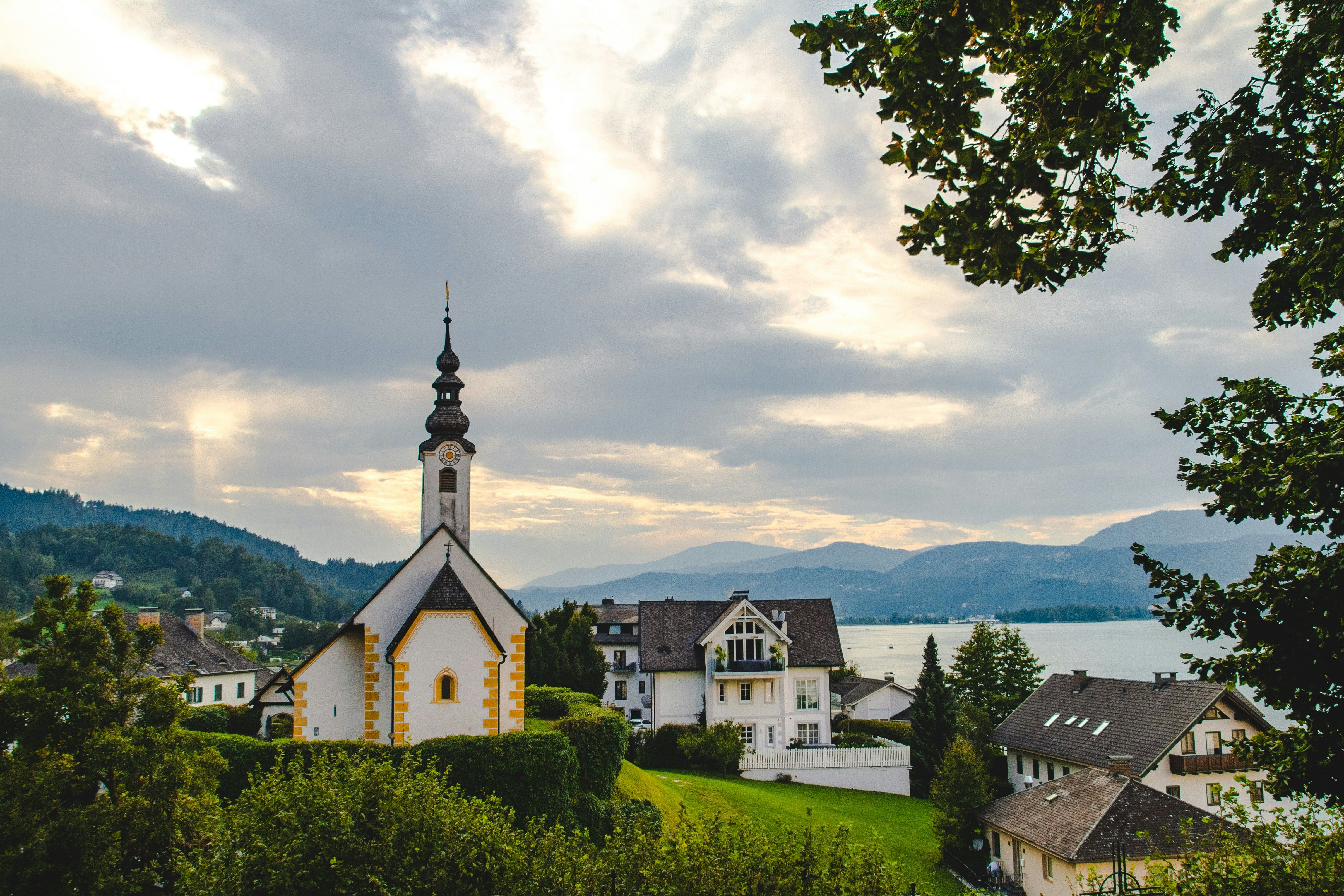 Dorf mit Kirche im Vordergrund und Berge und See im Hintergrund.