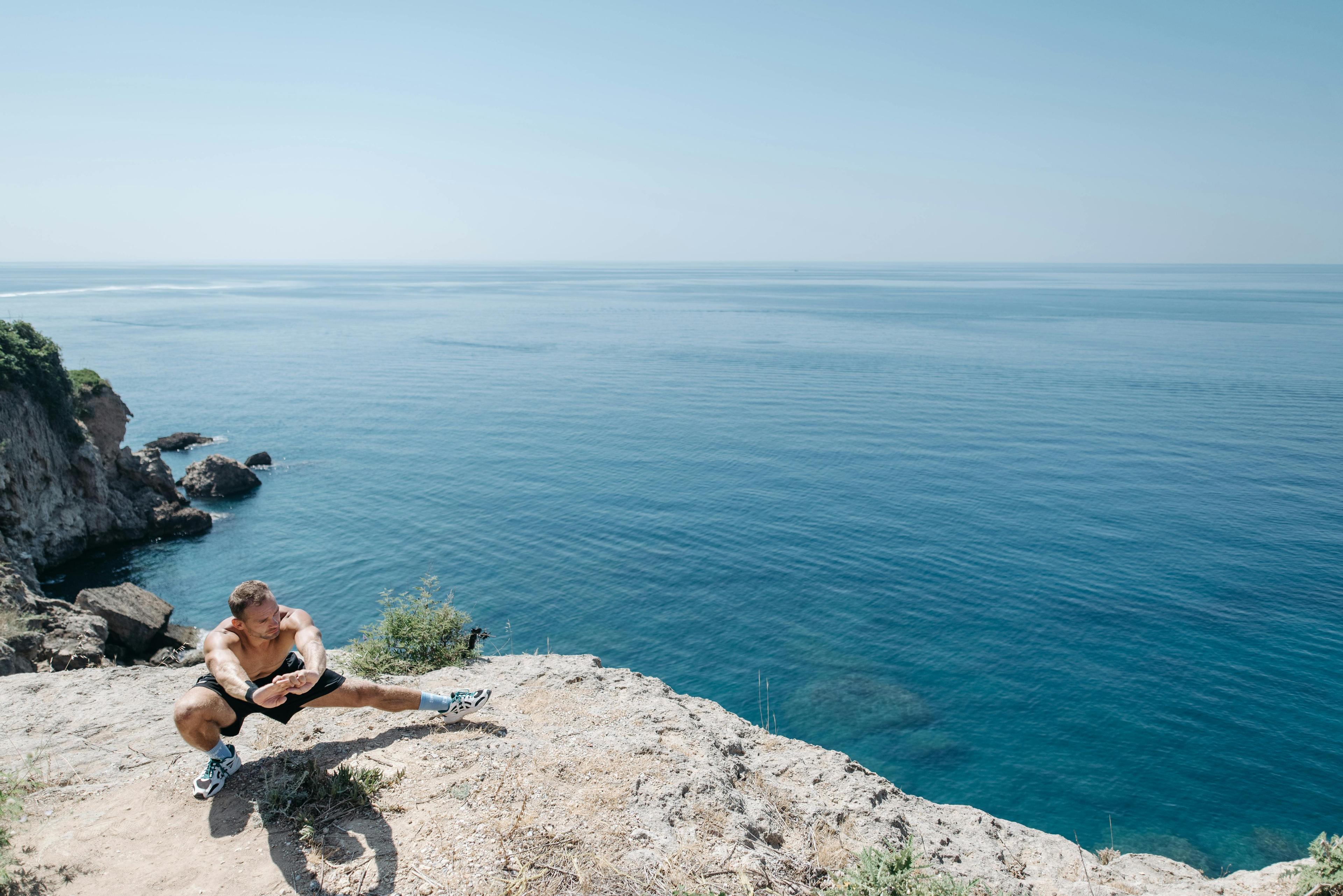 Person sitzt auf einem Felsen am Meer und blickt auf das Wasser