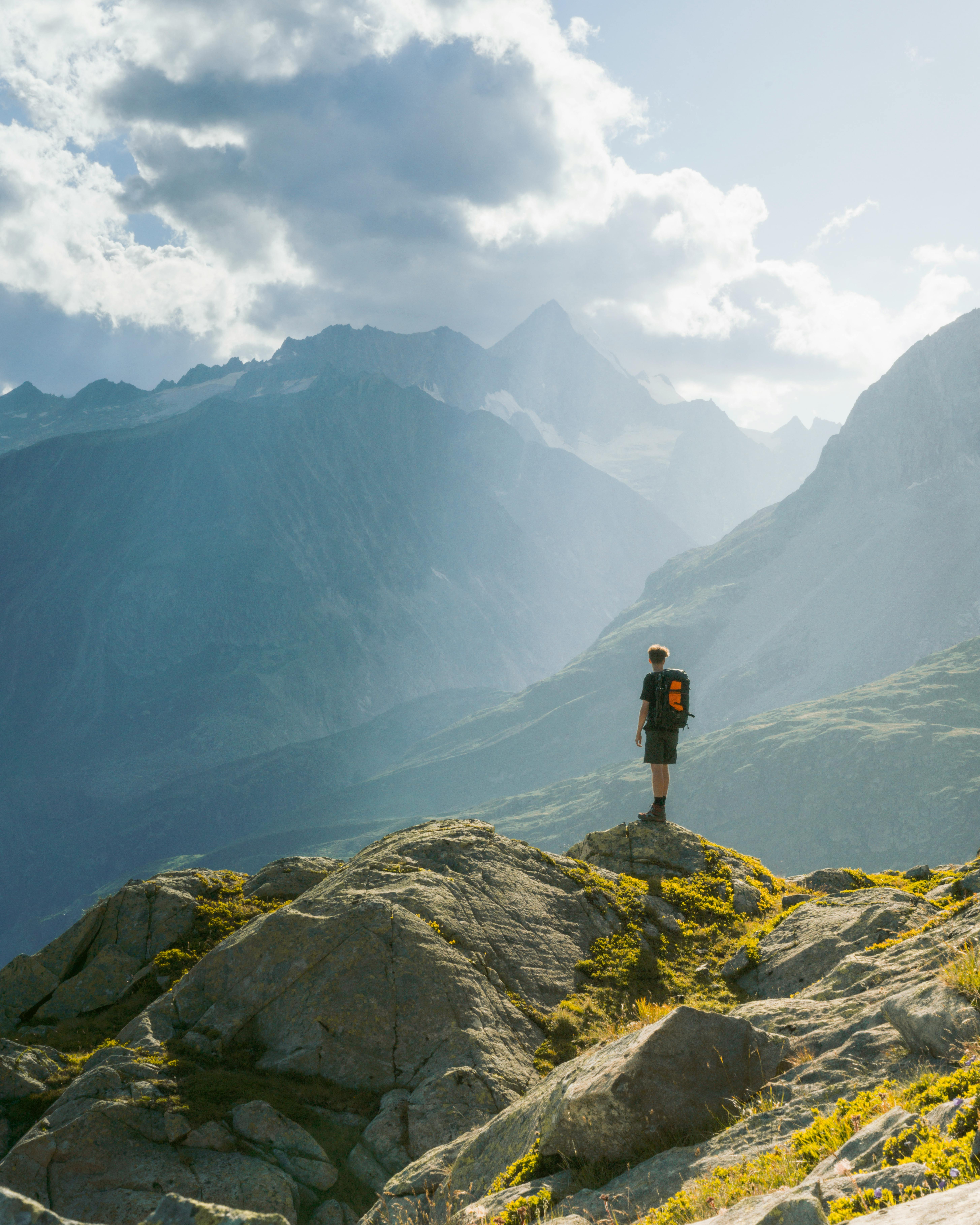 Person steht auf einem Berggipfel und blickt ins Tal