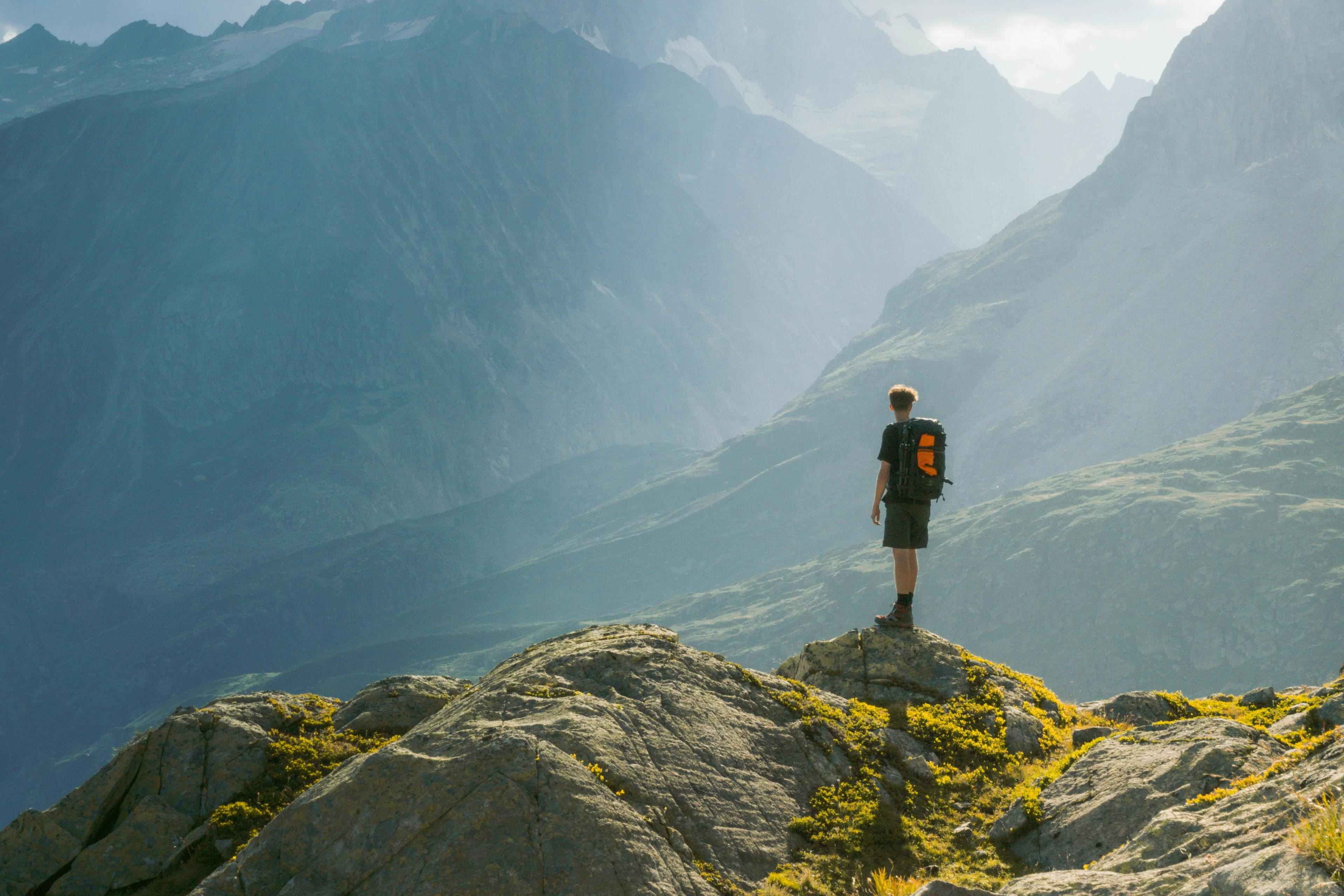 Person steht auf einem Berggipfel und blickt ins Tal