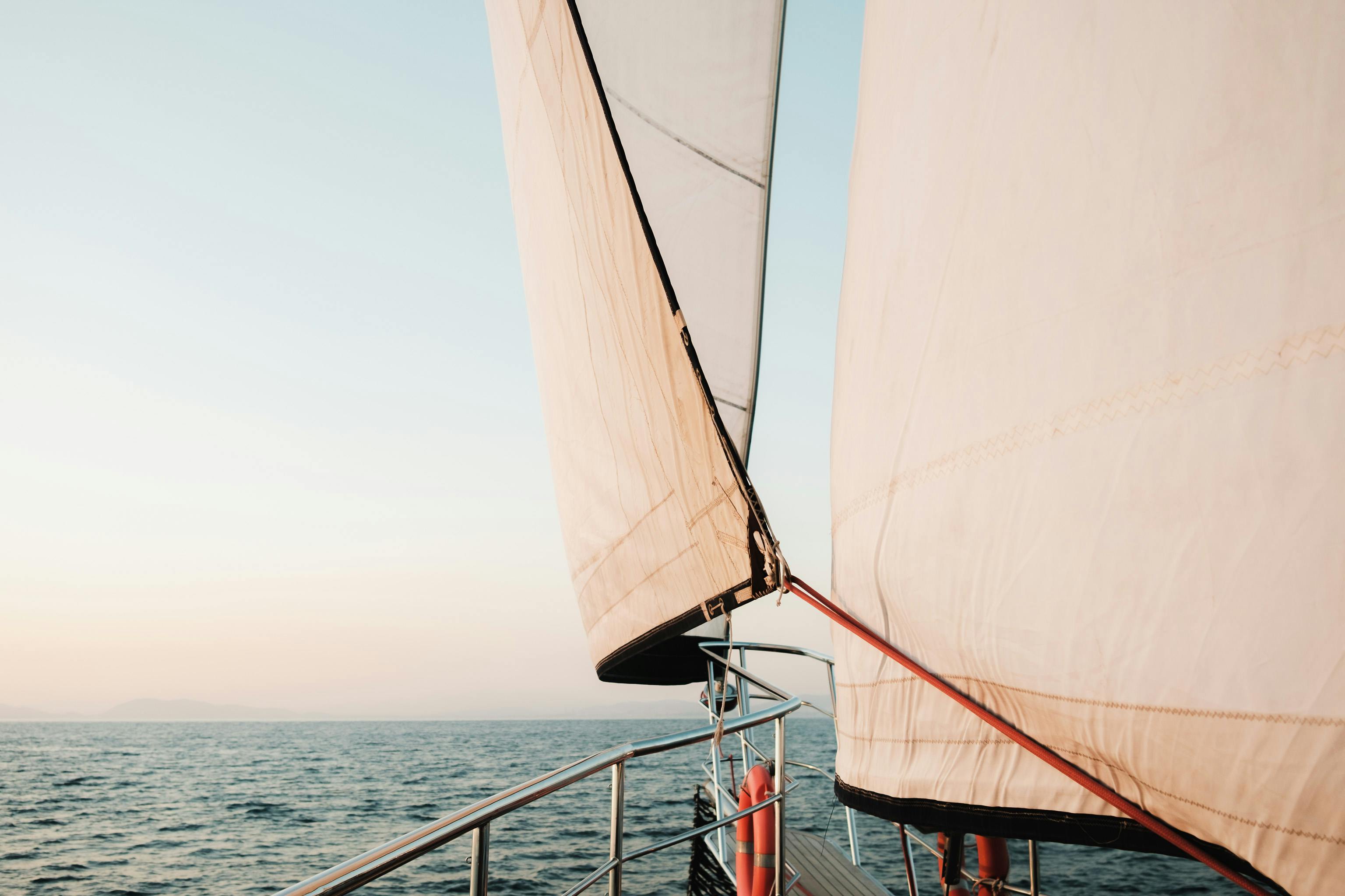 Nahaufnahme eines Segelboots, dessen Segel im Wind über dem Wasser gespannt sind.