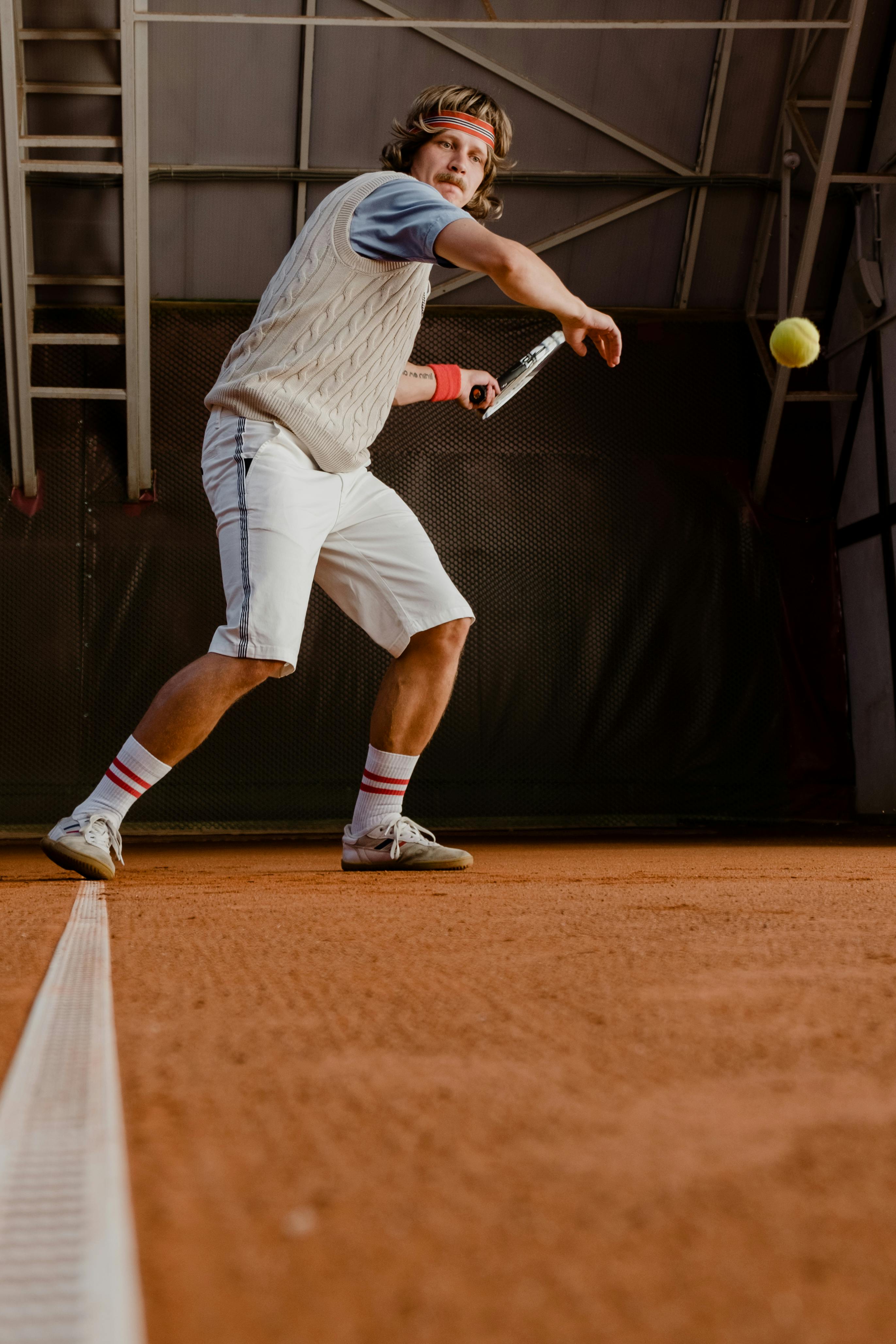 Männlicher Tennisspieler im weißen Outfit schlägt auf einem Sandplatz einen Ball