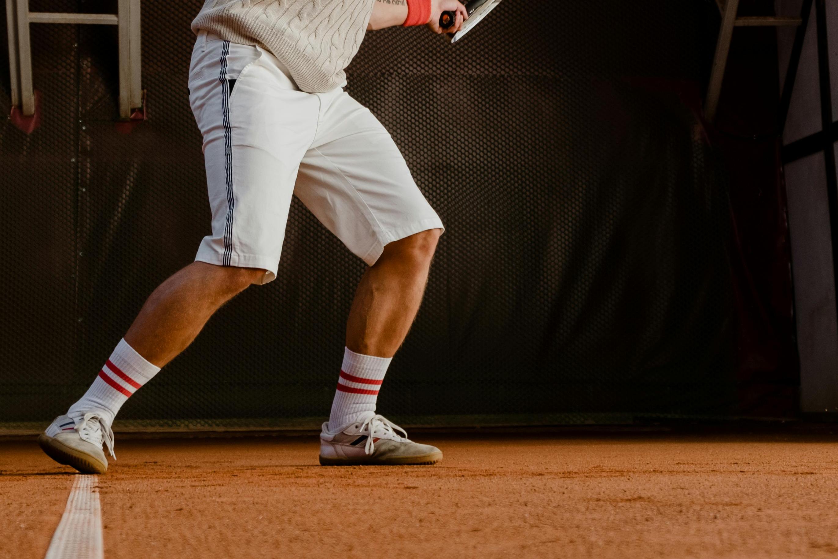 Männlicher Tennisspieler im weißen Outfit schlägt auf einem Sandplatz einen Ball