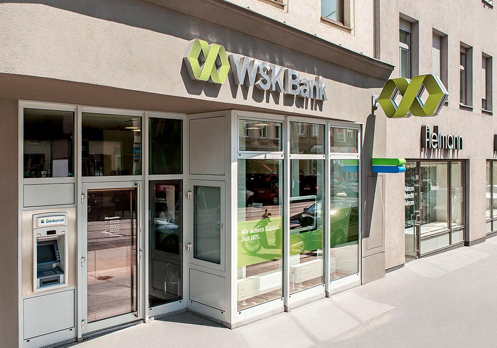 Eingangsbereich der WSK-Bank-Filiale Thaliastraße mit Geldautomat und großem Banklogo an der Gebäudefassade.