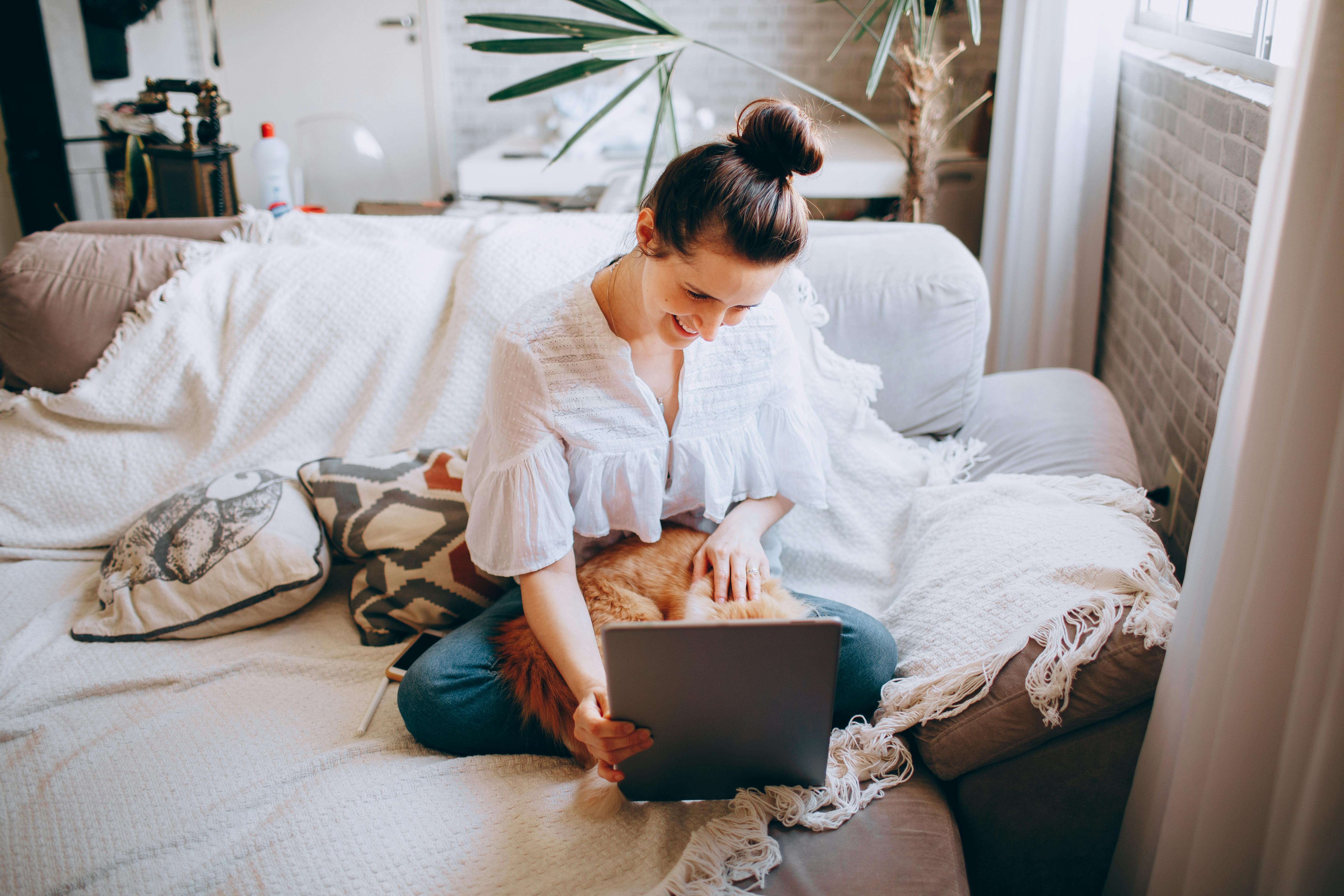 Eine Person sitzt entspannt auf einem Bett und arbeiten gemeinsam an einem Laptop.