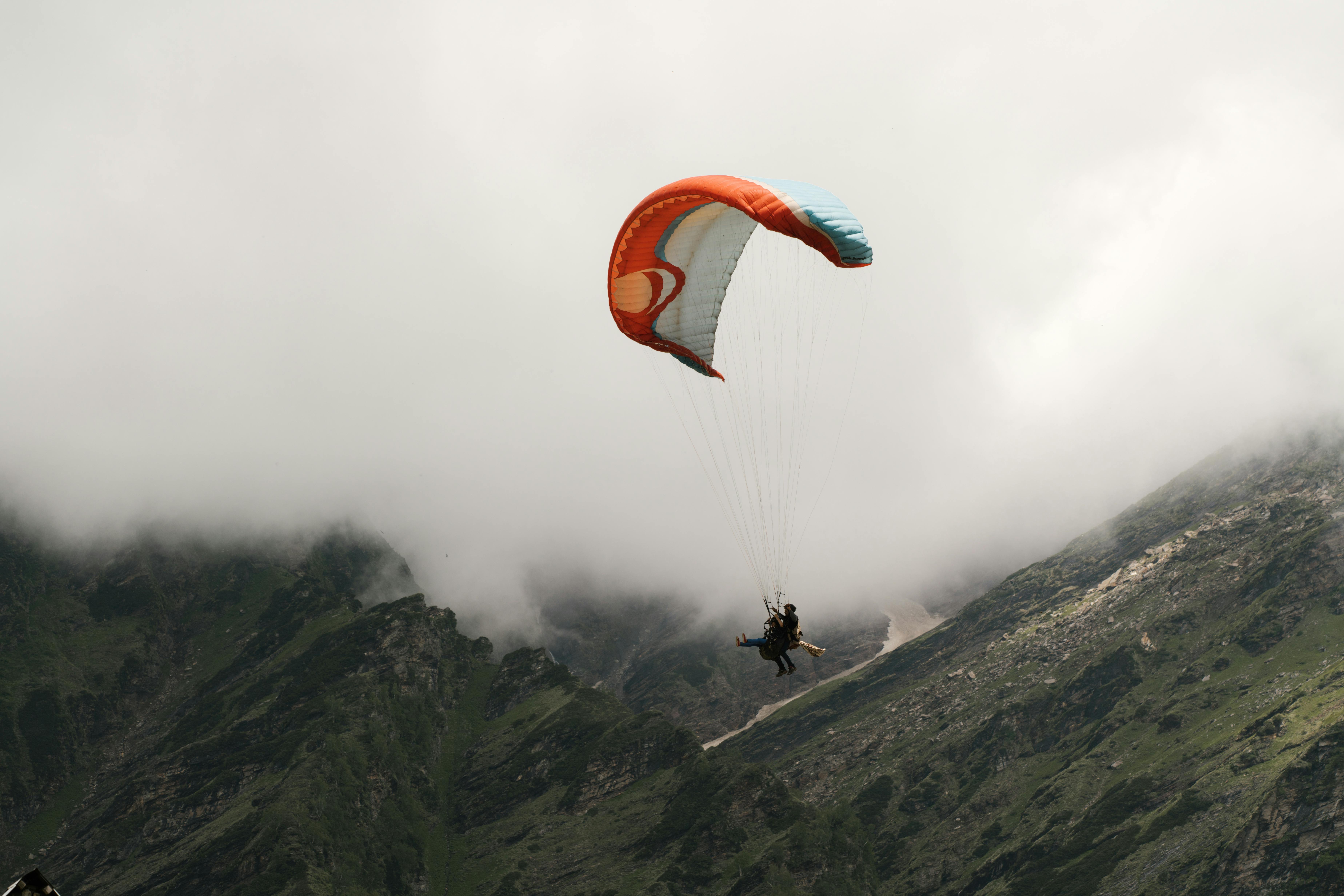 Paraglider schwebt über nebelverhangenen grünen Bergen.