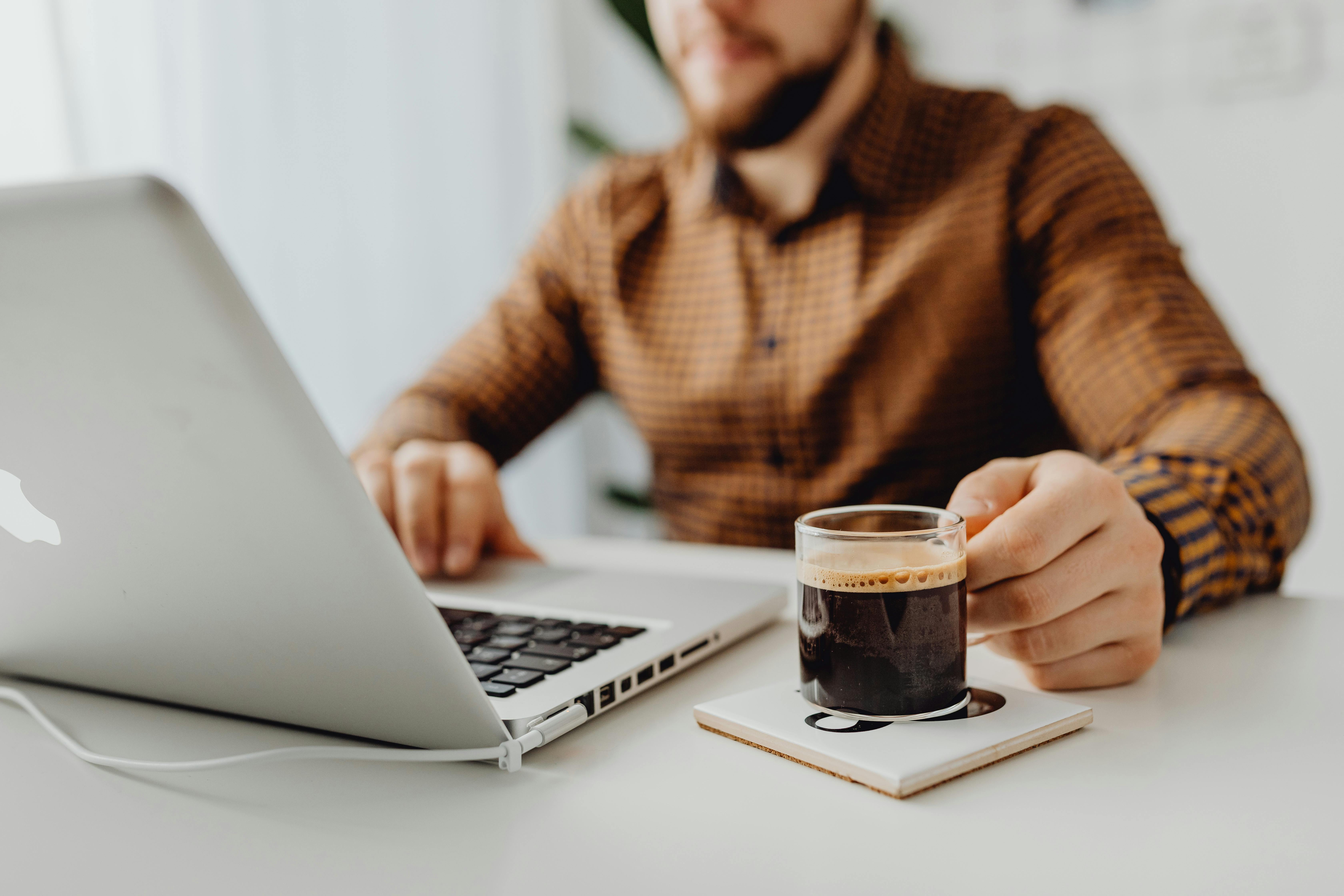 Person arbeitet auf Laptop mit einem Kaffee in der Hand.