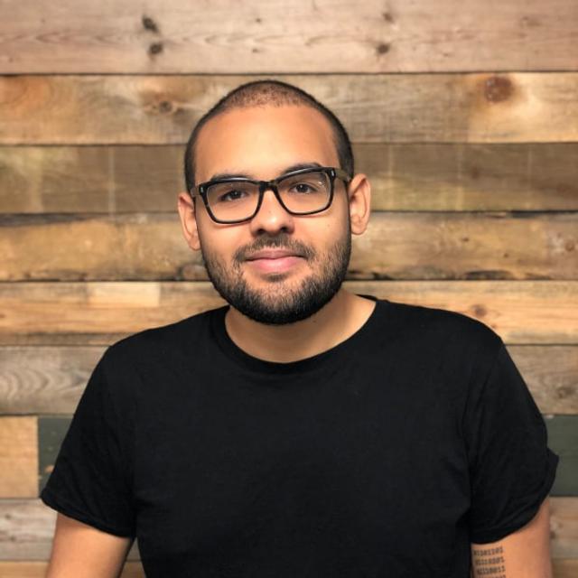 Man with glasses, dark hair and beard wearing a red t-shirt.