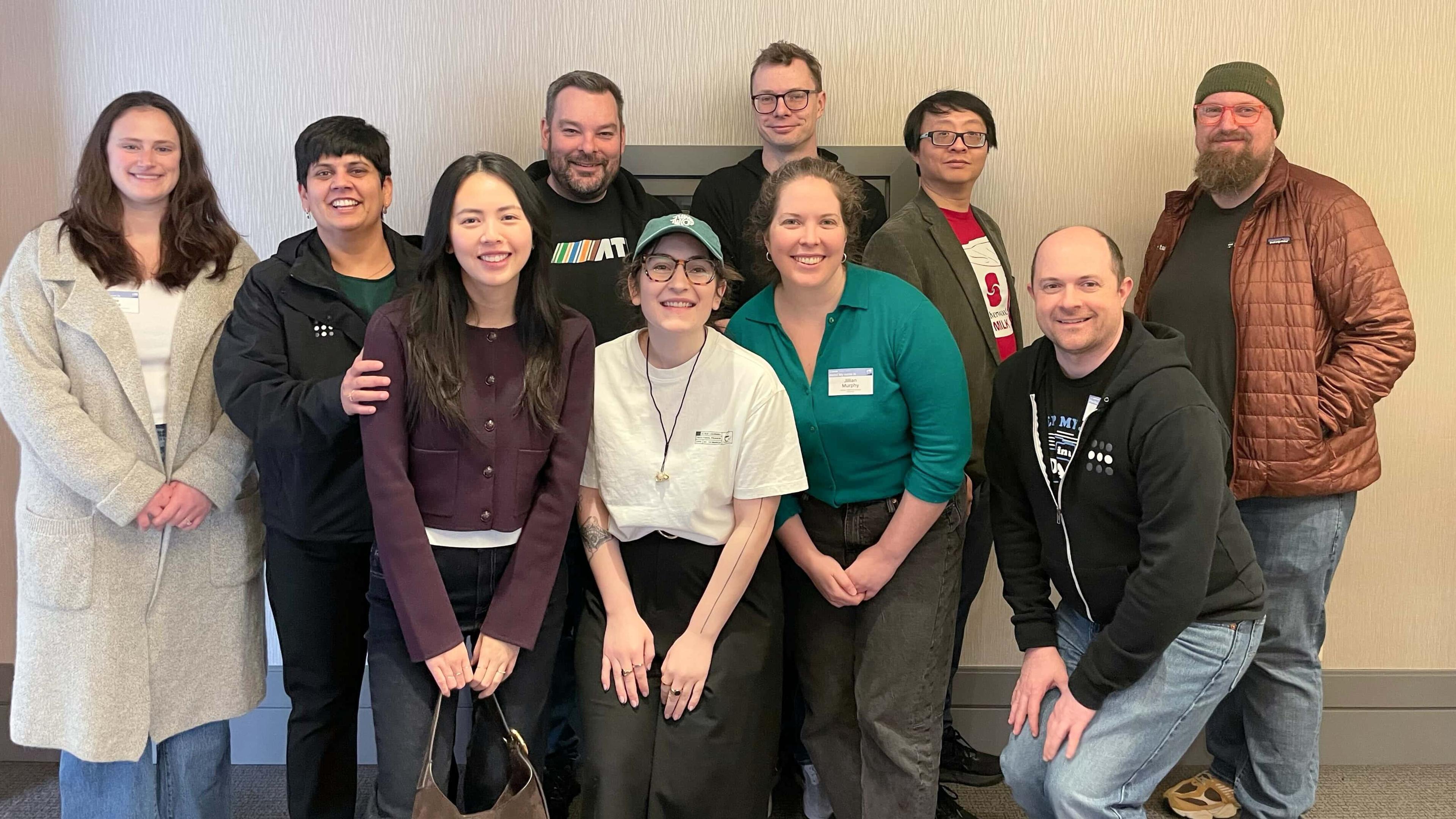 Tailscale employees, standing against a beige wall, roughly half of them wearing Tailscale shirts and hoodies.
