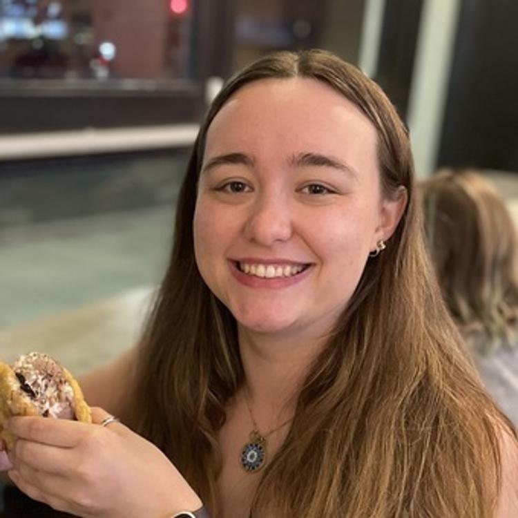 Image of Megan Walsh, in front of a window facing the street, holding an ice cream cookie sandwich.