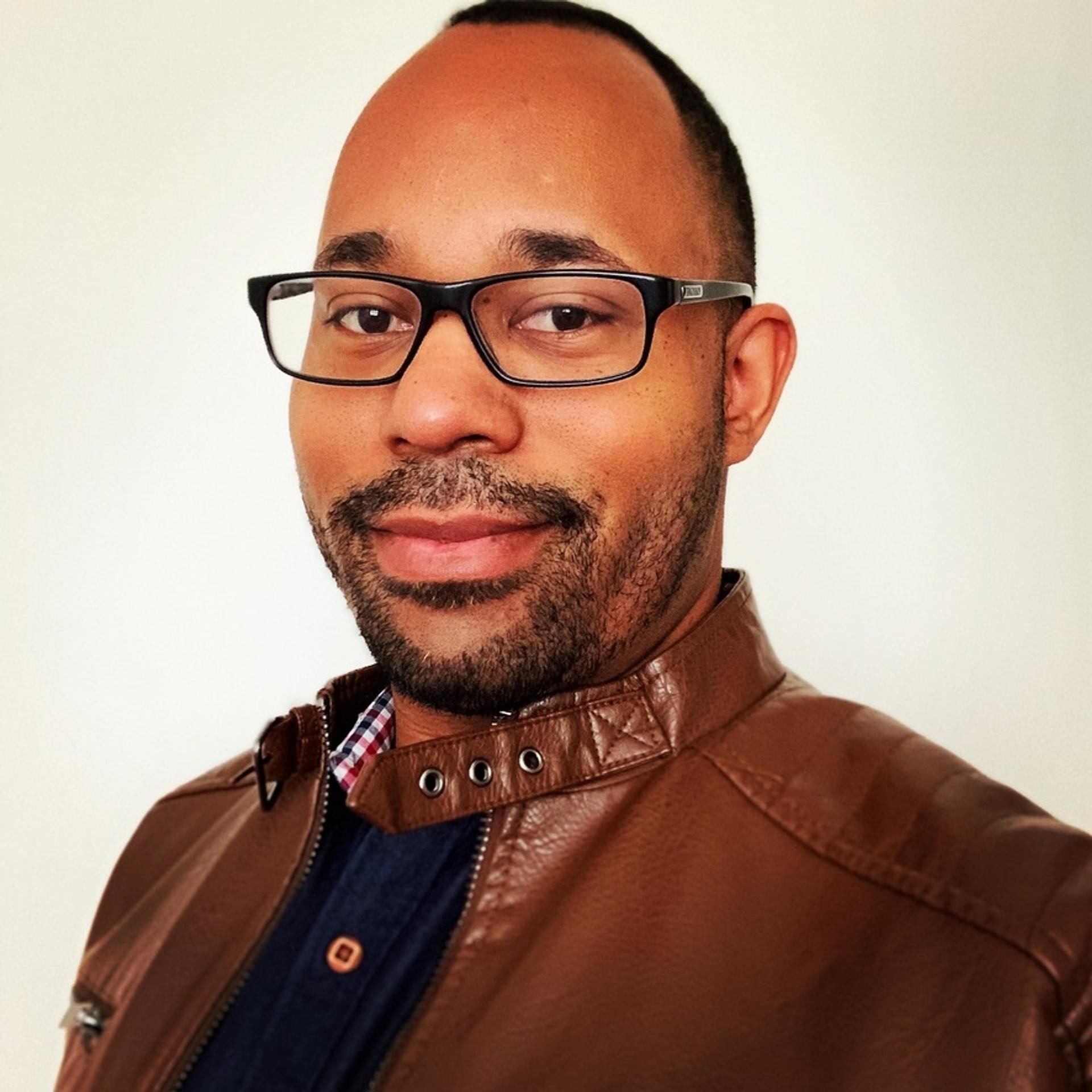 Image of Brian Scott, with glasses, wearing a leather jacket over a blue sweater.