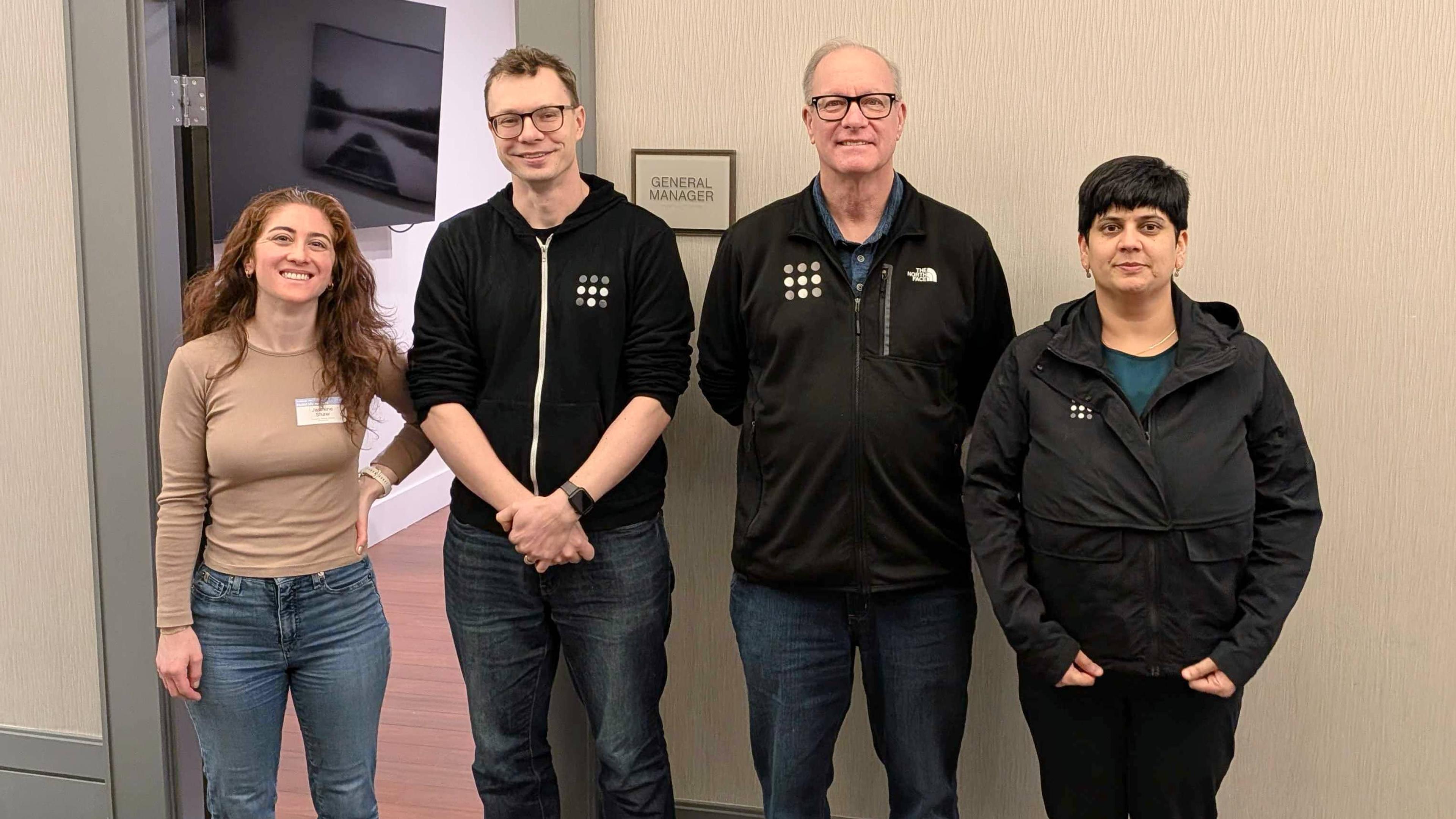 Four Tailscale employees, standing against a beige wall with a door open behind them to the left.