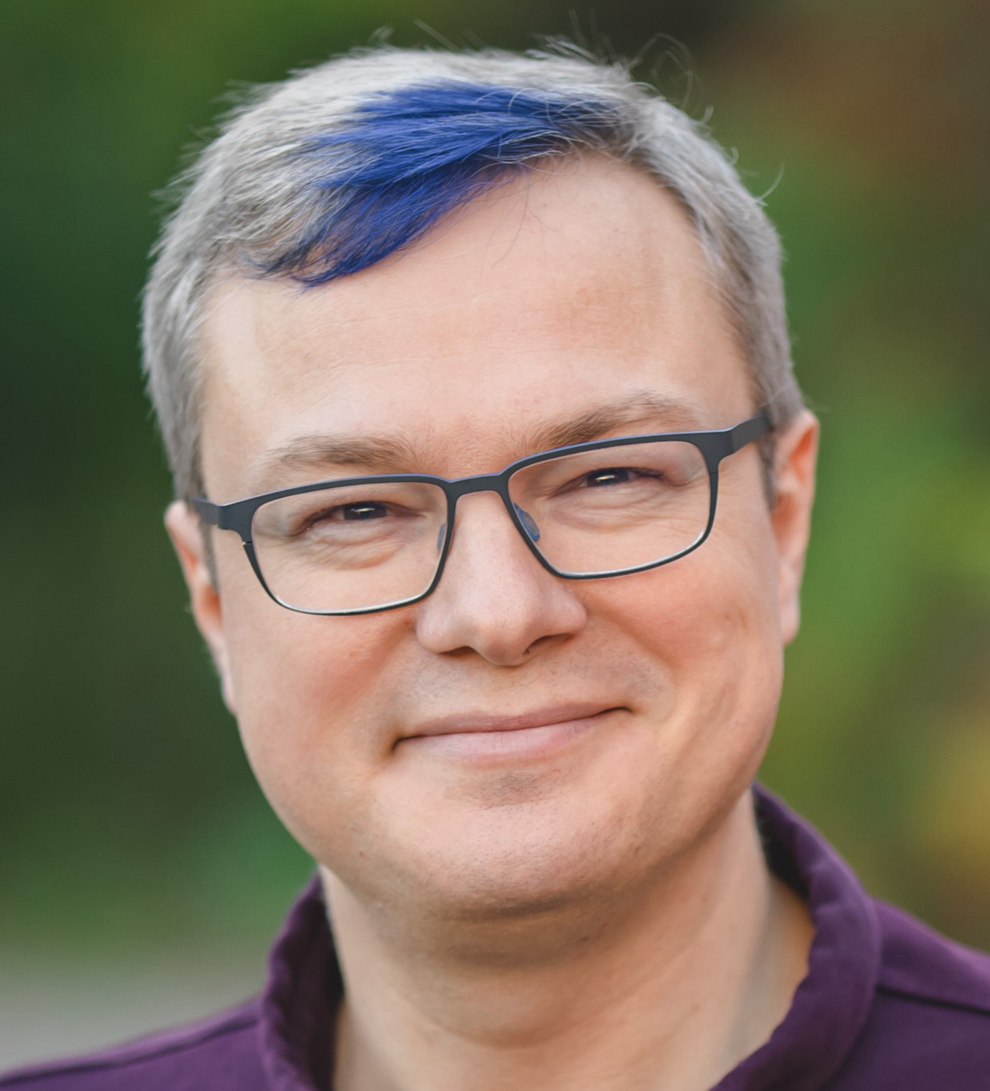 Image of Mike Shaver, wearing glasses, a purple polo shirt and a shock of blue hair across the front of his hair.