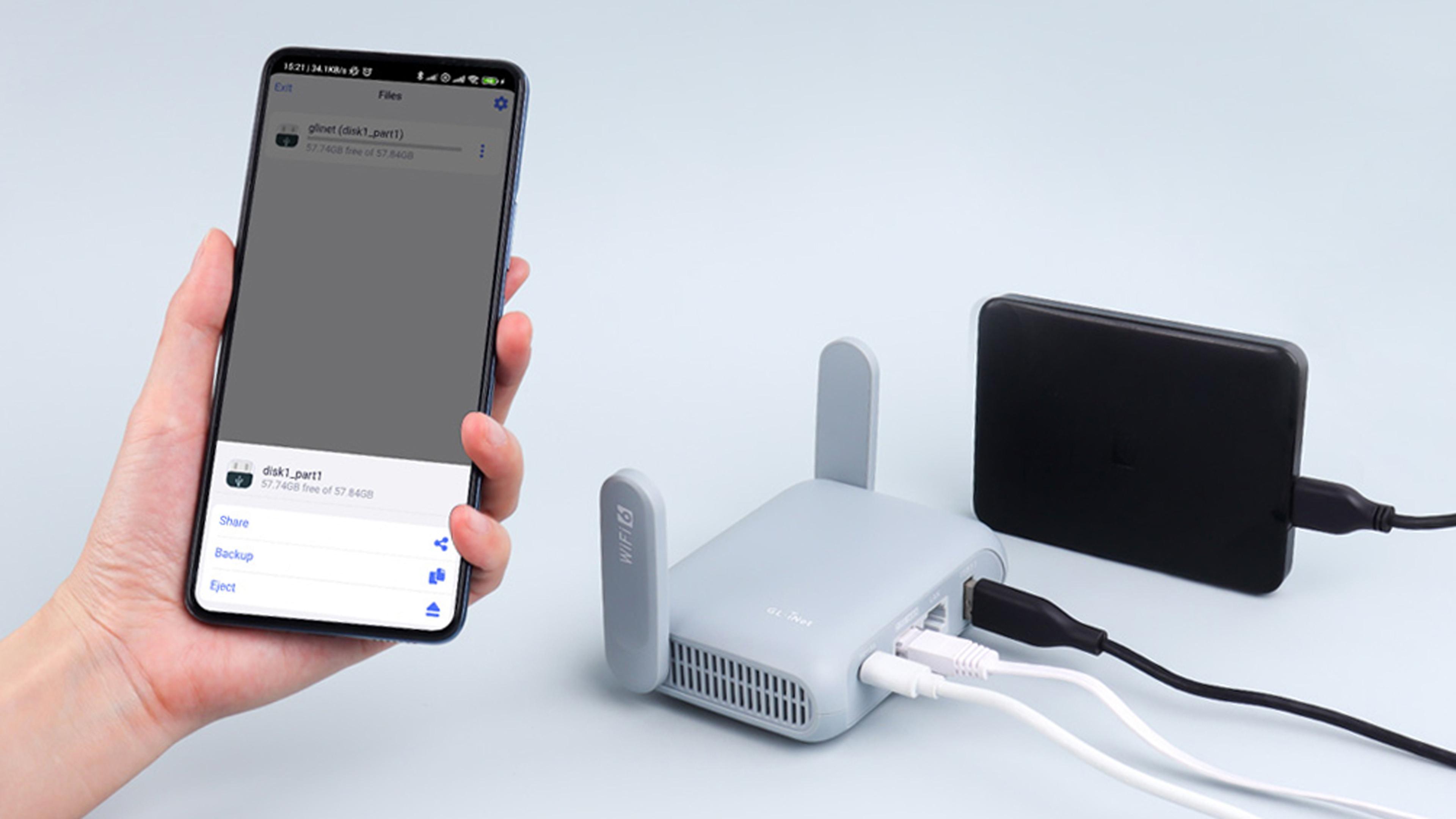 A phone held in a hand, with "Share, Backup, Eject" options showing, for a travel router that has a portable USB drive plugged into it, along with power and ethernet cables.