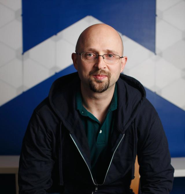 Man wearing glasses with a beard in front of a blue and white background.