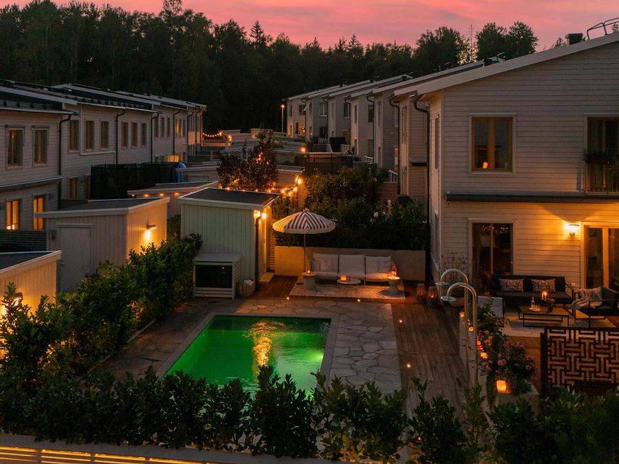 Uteplatsen i skymningen med belyst pool och varm fasadbelysning