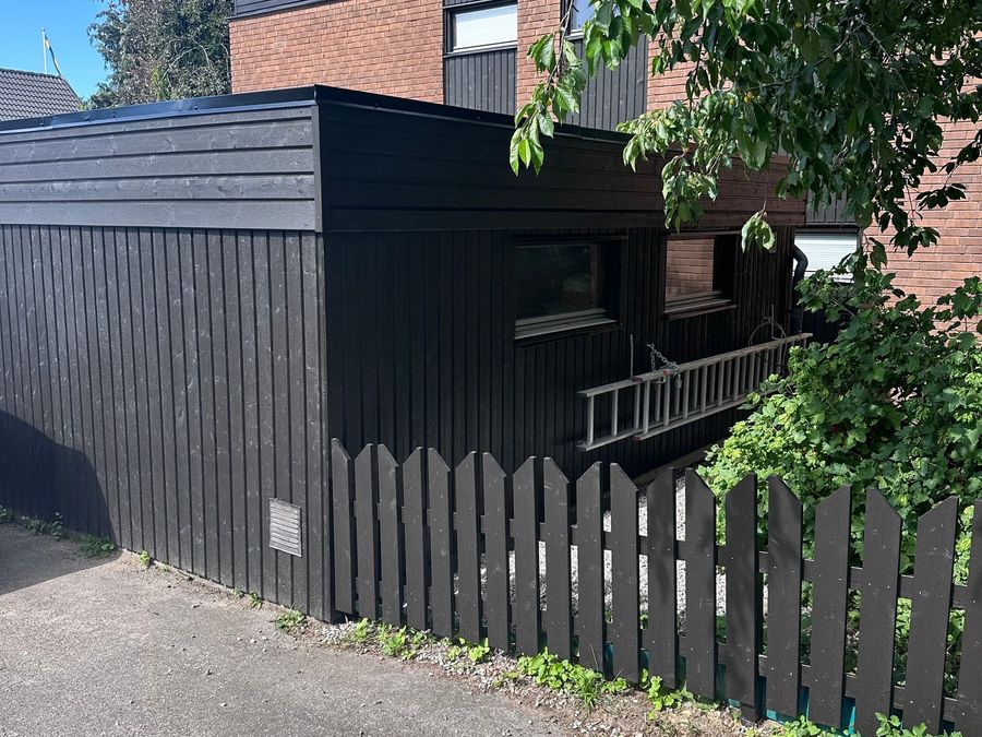 Nymålad mörk träpanel och nytt staket efter fasadrenoveringen
