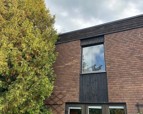 Huset före renoveringen, brunt tegel och sliten mörk träpanel under fönstren
