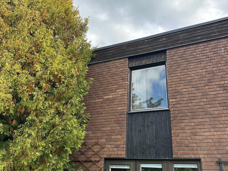 Huset före renoveringen, brunt tegel och sliten mörk träpanel under fönstren