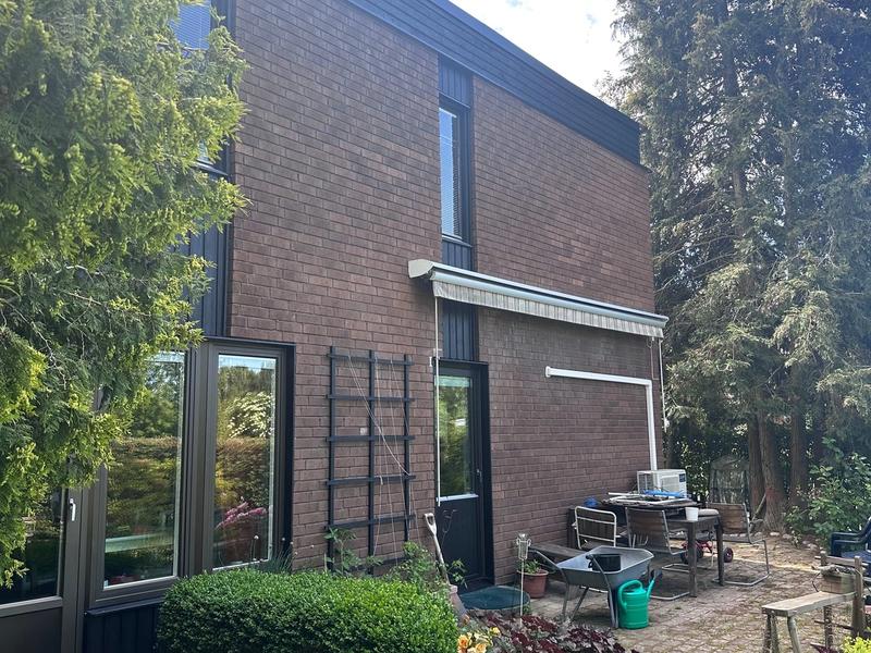 Renoverat hus i Hässelby en sommardag, brunt tegel och nymålad mörk träpanel
