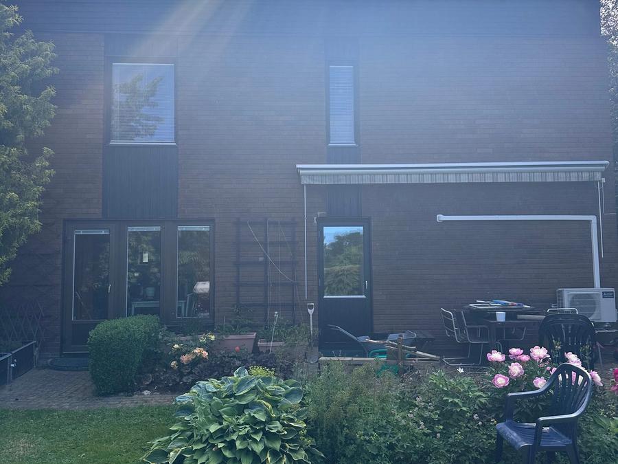 Husets baksida efter renoveringen med nymålad panel och trädgård i sommarskrud