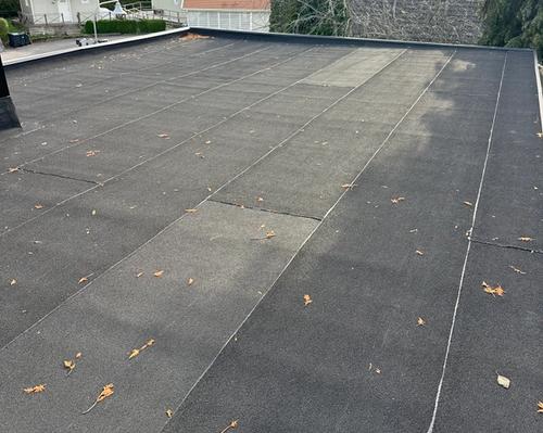 Gammalt spräckt papptak före renovering, tydliga sprickor och slitage