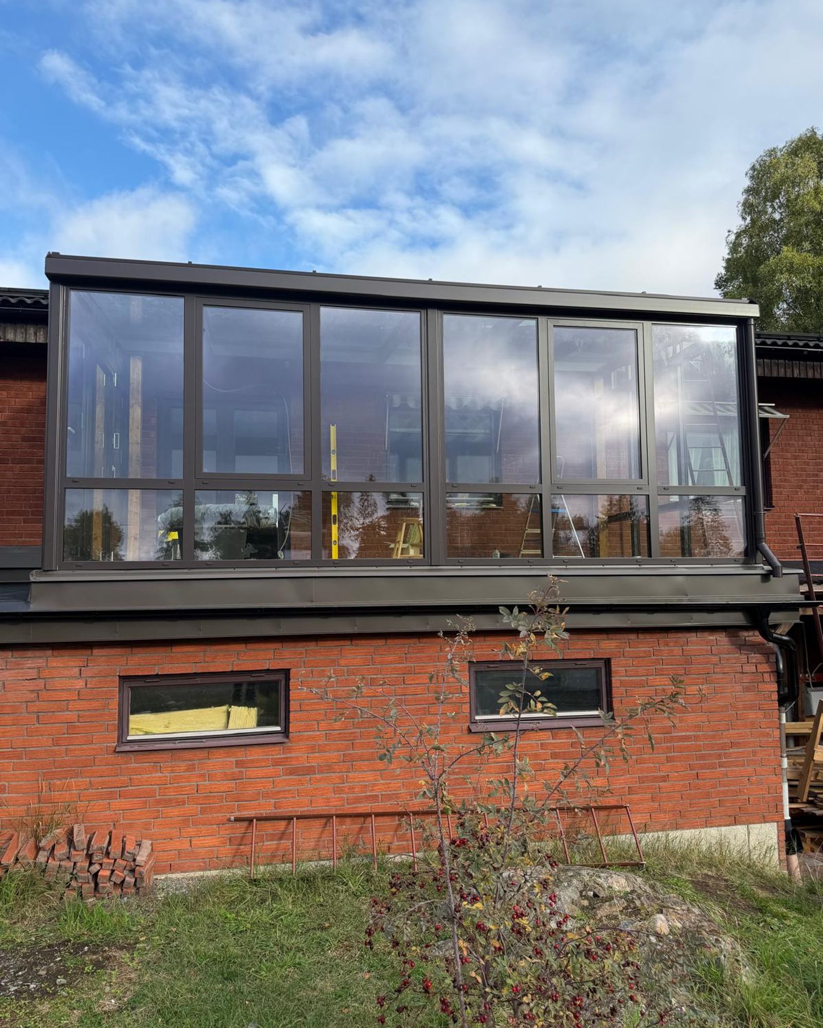 Inglasad terrass på ombyggt garagetak i Huddinge, med tegelfasad och mörka plåtbeslag