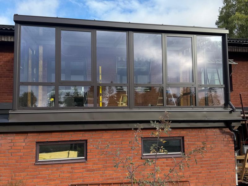 Inglasad terrass på ombyggt garagetak i Huddinge, med tegelfasad och mörka plåtbeslag