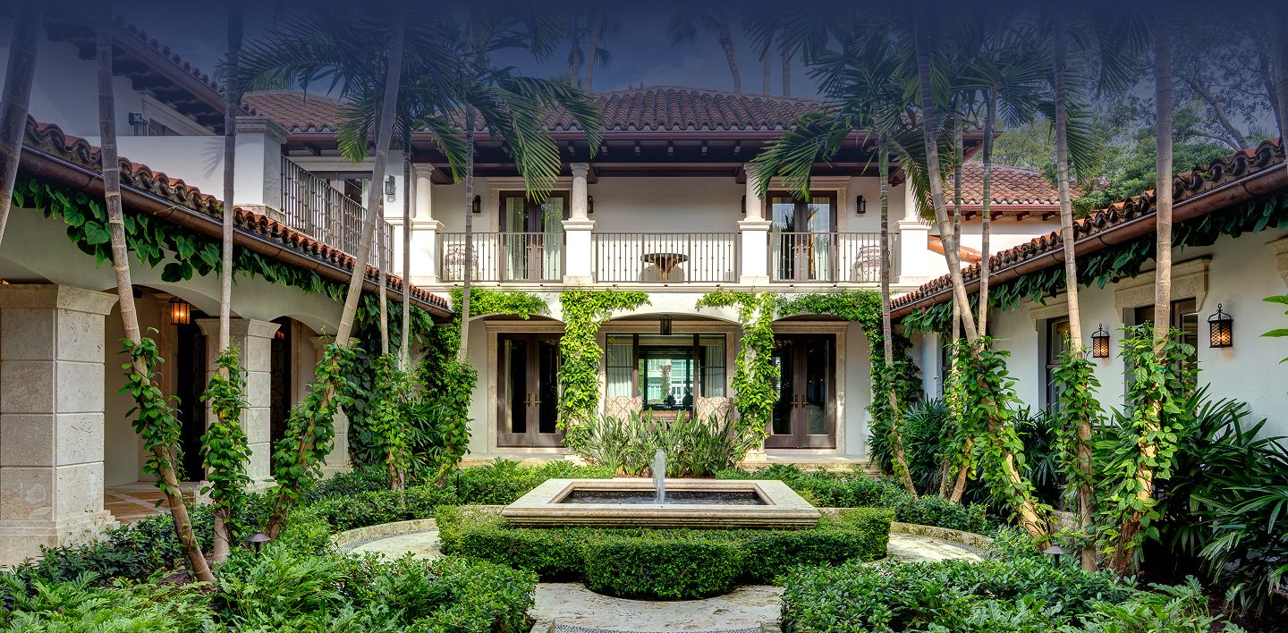 Spanish-style courtyard estate with terracotta tile roof, soaring palm trees, and a central stone fountain surrounded by lush gardens in Miami