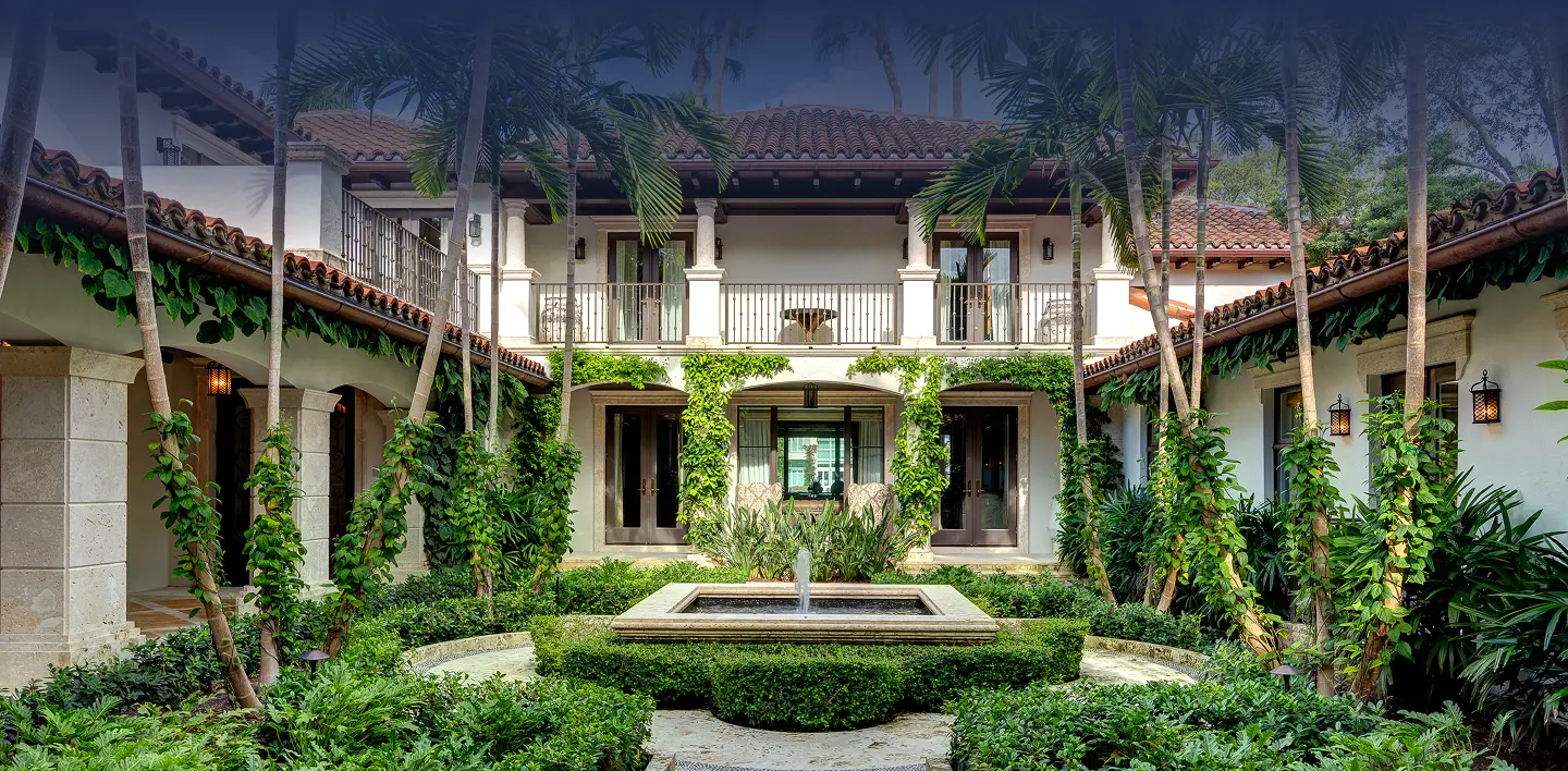 Spanish-style courtyard estate with terracotta tile roof, soaring palm trees, and a central stone fountain surrounded by lush gardens in Miami