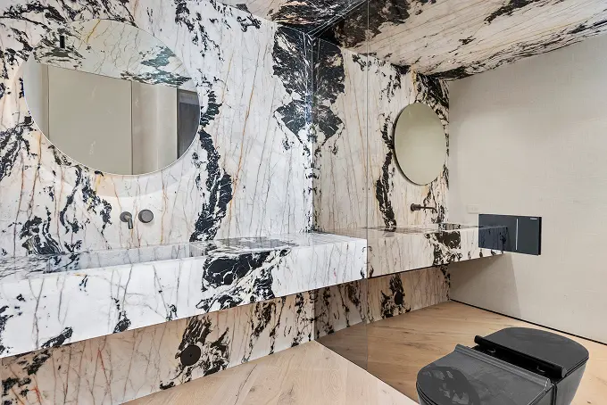 Modern bathroom finished in black and white marble with a large glass mirror wall.