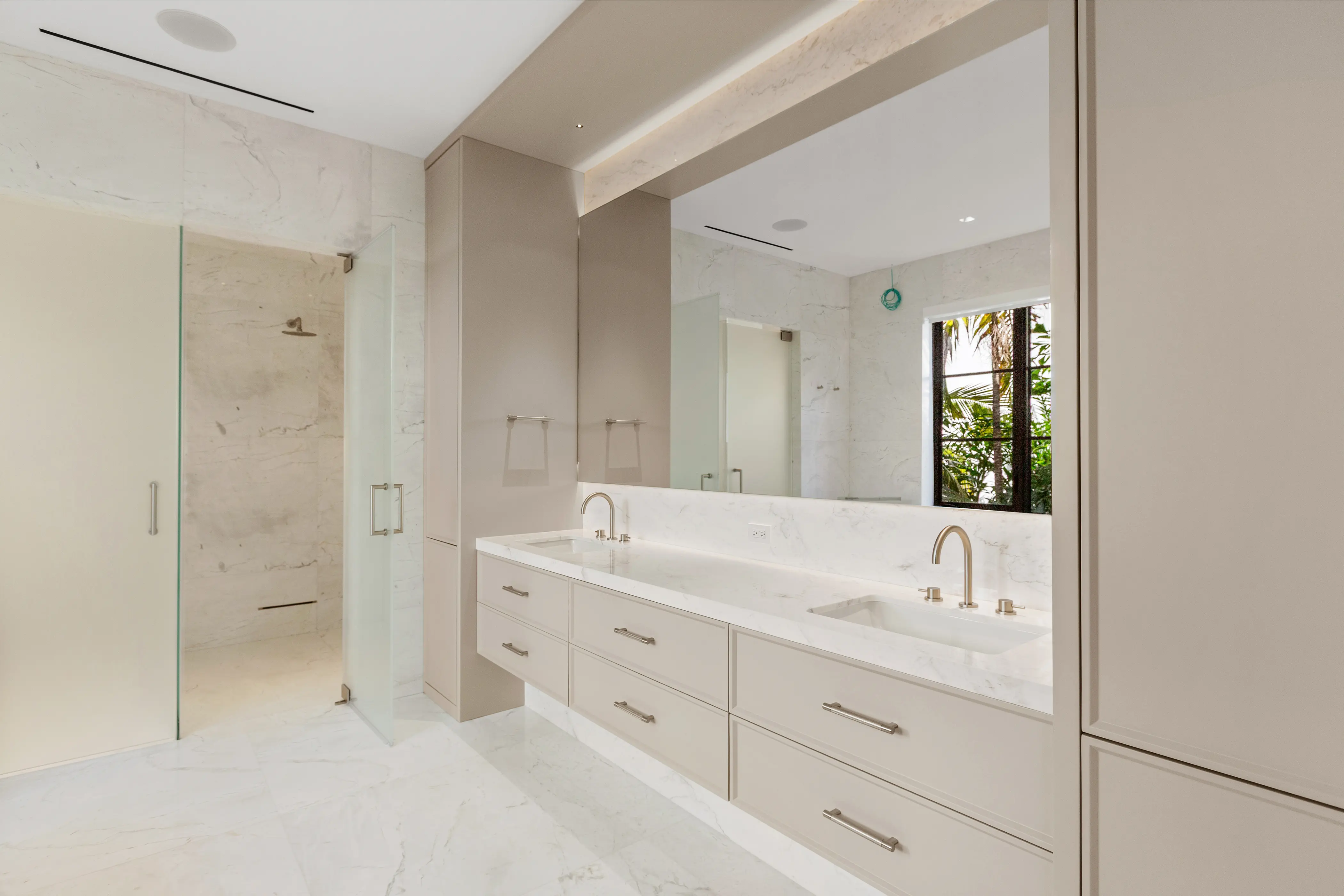 Bright luxury bathroom featuring a custom double vanity, marble surfaces, integrated storage, glass shower enclosure, and minimalist contemporary fixtures.