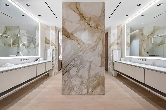 Split master bathroom featuring dual vanities with large illuminated mirrors.