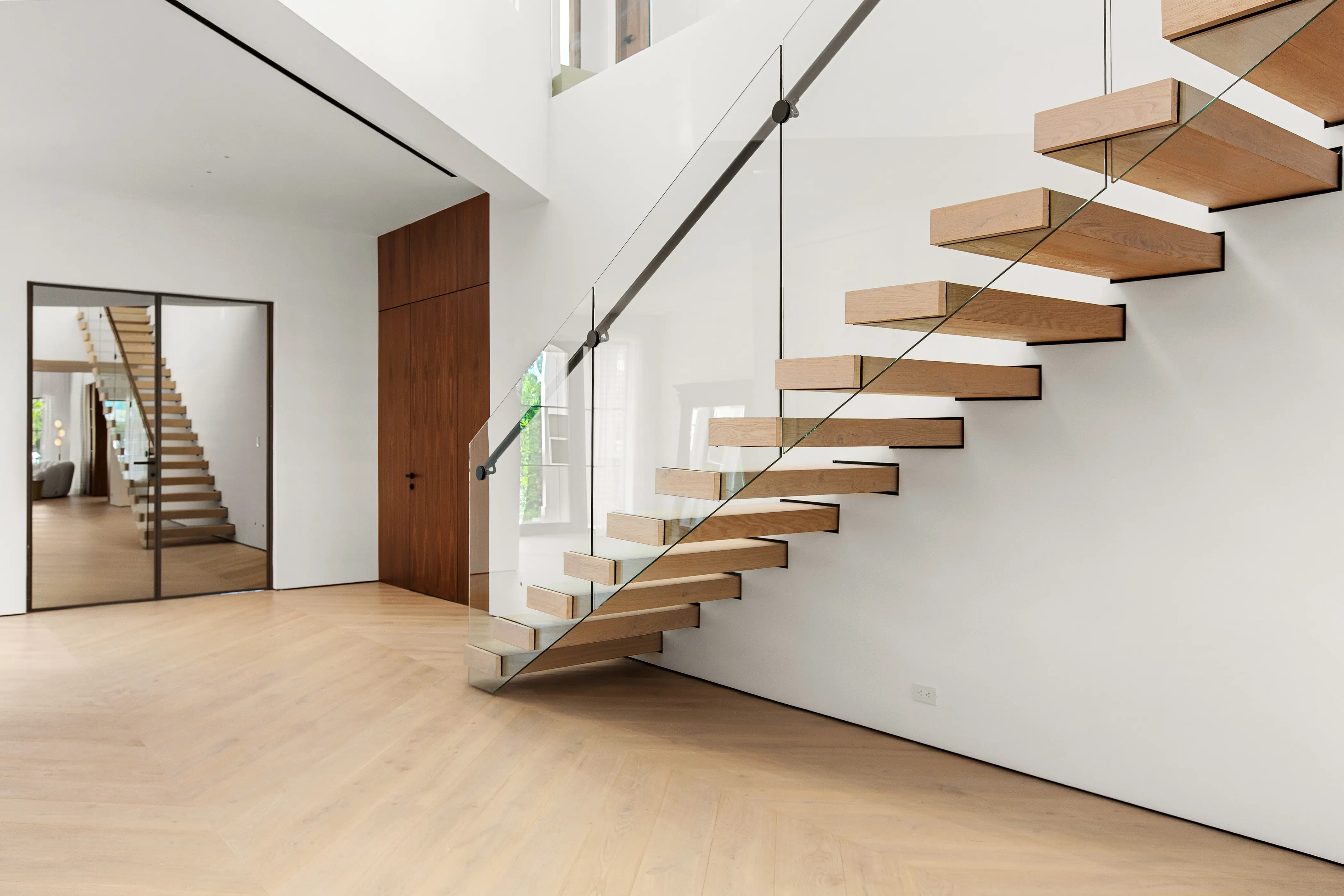 Contemporary floating staircase featuring wood treads, a glass railing, minimalist detailing, and clean architectural lines in a luxury residence.