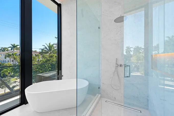Modern white marble bathroom with a soaking tub, a large glass shower, and window views.