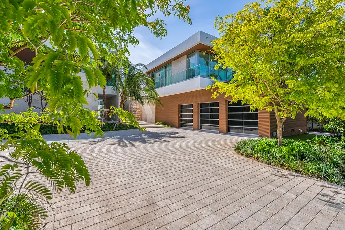 Modern house courtyard with a glass garage, framed by mature tree-lined landscaping.